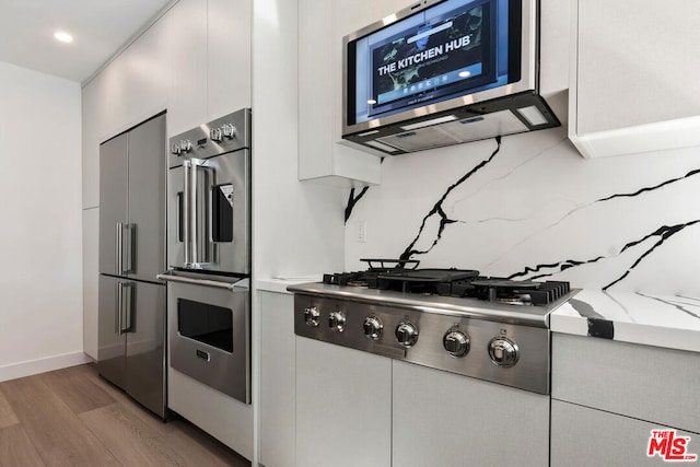 kitchen featuring appliances with stainless steel finishes, white cabinetry, decorative backsplash, light hardwood / wood-style floors, and light stone countertops