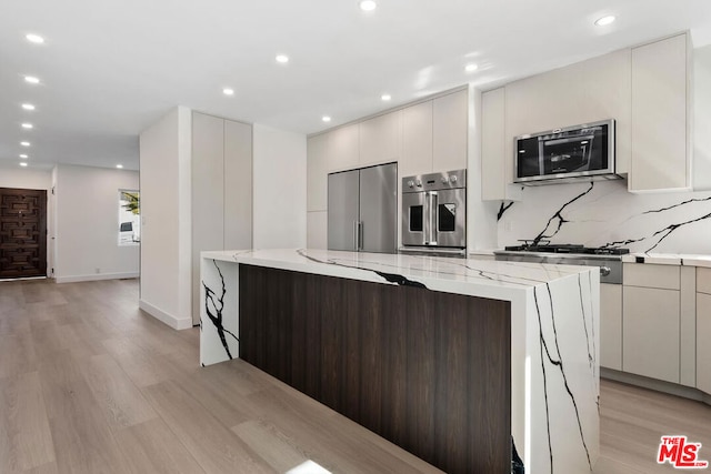 kitchen with light stone counters, backsplash, light hardwood / wood-style flooring, and appliances with stainless steel finishes