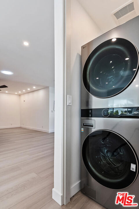 laundry area with stacked washer and clothes dryer and light wood-type flooring