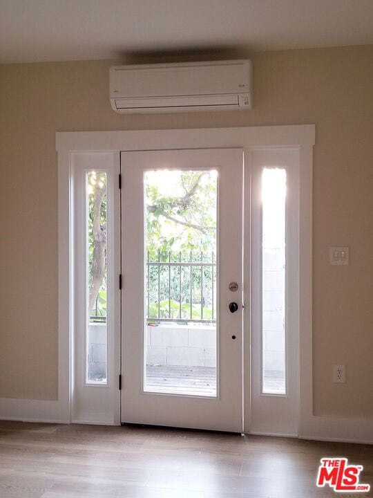 doorway with a wall unit AC and light hardwood / wood-style floors