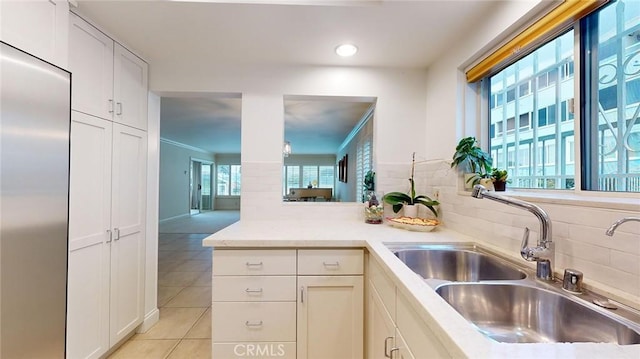 kitchen with sink, tasteful backsplash, light tile patterned floors, stainless steel built in fridge, and white cabinets