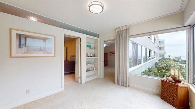 spare room featuring built in shelves and light carpet