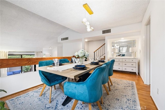 dining room with vaulted ceiling, a textured ceiling, and light wood-type flooring