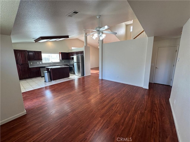 unfurnished living room with ceiling fan, vaulted ceiling, light hardwood / wood-style flooring, and a textured ceiling