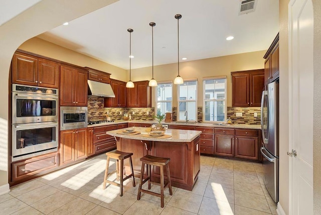 kitchen featuring a breakfast bar, decorative light fixtures, a center island, stainless steel appliances, and light stone countertops