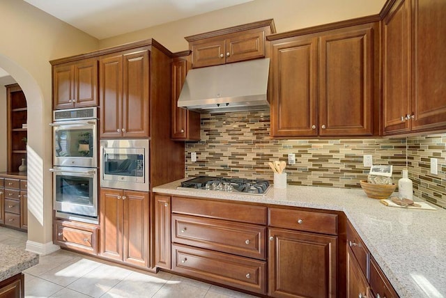 kitchen featuring appliances with stainless steel finishes, ventilation hood, tasteful backsplash, light tile patterned floors, and light stone counters