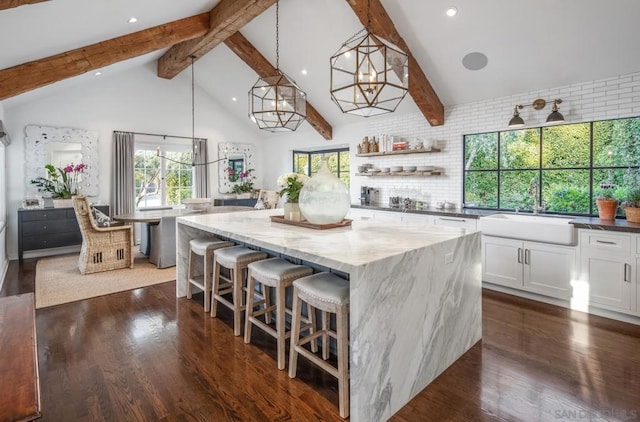 kitchen with sink, a kitchen island, pendant lighting, dark stone counters, and white cabinets