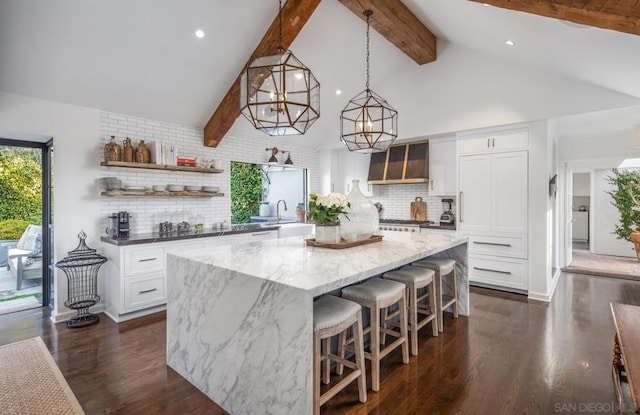 kitchen featuring decorative light fixtures, white cabinetry, dark stone countertops, a center island, and beam ceiling