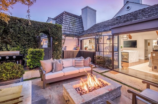 patio terrace at dusk featuring area for grilling and an outdoor living space with a fire pit