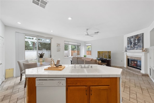 kitchen with sink, tile counters, dishwasher, and a center island with sink