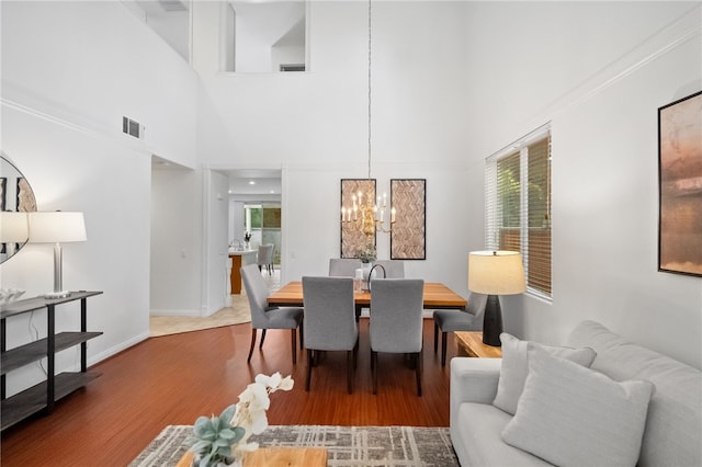 dining area featuring hardwood / wood-style flooring, a towering ceiling, and a notable chandelier