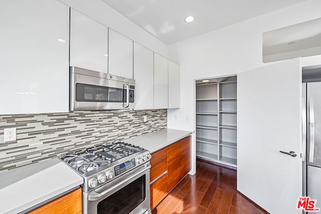 kitchen with stainless steel appliances, dark wood-type flooring, white cabinets, and backsplash