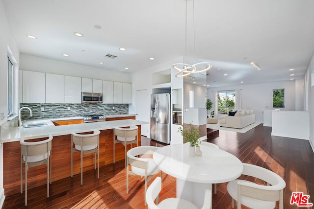 kitchen featuring appliances with stainless steel finishes, pendant lighting, white cabinetry, sink, and backsplash