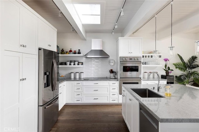 kitchen featuring wall chimney exhaust hood, sink, white cabinetry, decorative light fixtures, and appliances with stainless steel finishes