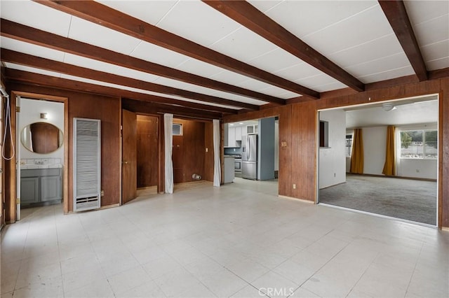 unfurnished living room featuring beam ceiling and wooden walls