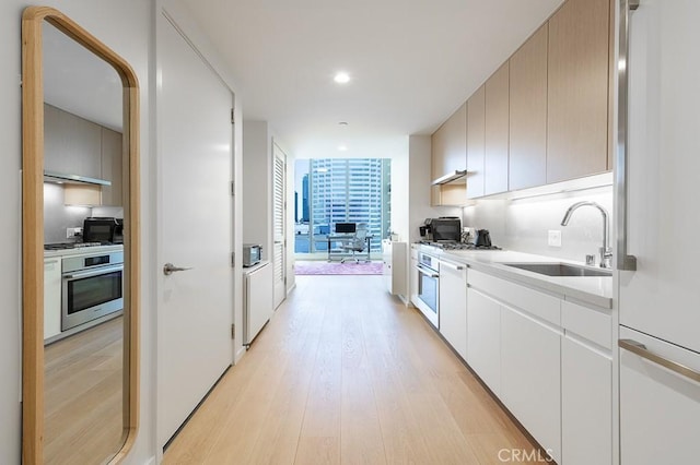 kitchen with expansive windows, a sink, oven, and light wood-style floors