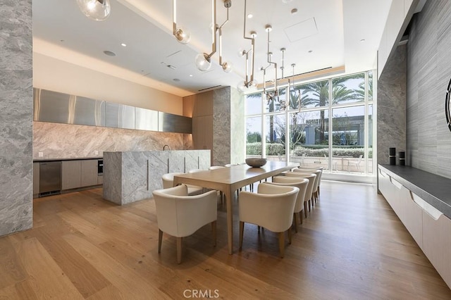 dining space featuring floor to ceiling windows, a towering ceiling, and light wood finished floors