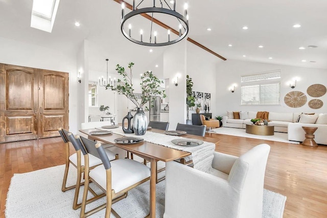 dining space featuring high vaulted ceiling, a notable chandelier, light wood-type flooring, and a skylight