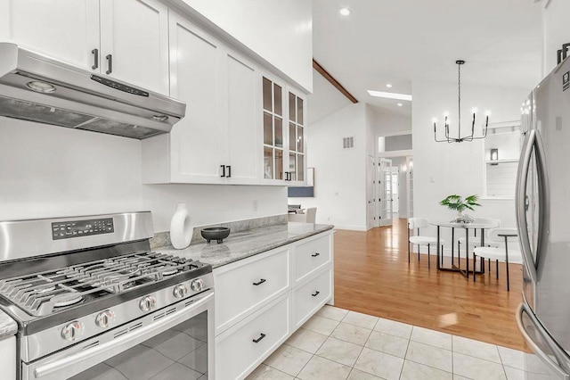 kitchen with light tile patterned floors, appliances with stainless steel finishes, a notable chandelier, light stone countertops, and white cabinets