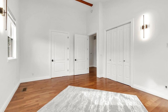 unfurnished bedroom with hardwood / wood-style floors, a closet, and a high ceiling