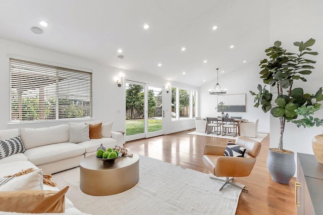 living room with lofted ceiling, an inviting chandelier, and light hardwood / wood-style flooring