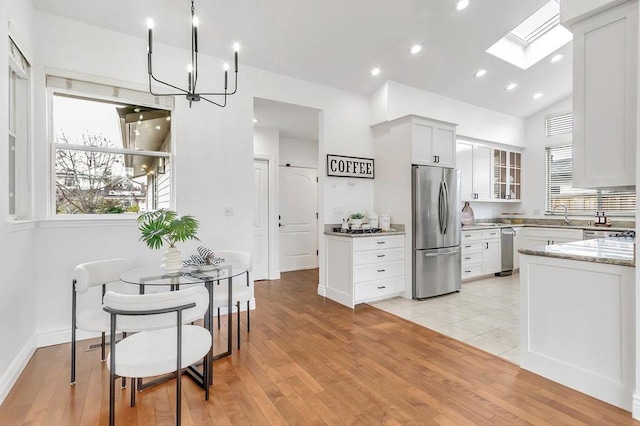 kitchen with white cabinetry, appliances with stainless steel finishes, light stone counters, and light hardwood / wood-style flooring