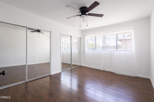 unfurnished bedroom featuring multiple closets, dark hardwood / wood-style floors, and ceiling fan