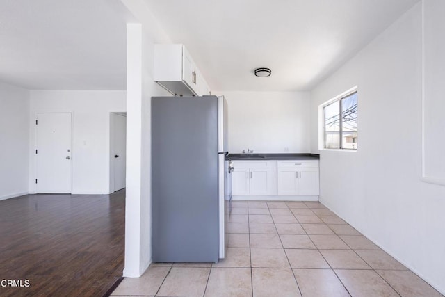 kitchen with white cabinetry, sink, stainless steel fridge, and light tile patterned flooring