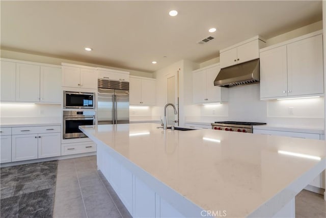 kitchen featuring built in appliances, sink, white cabinetry, and an island with sink