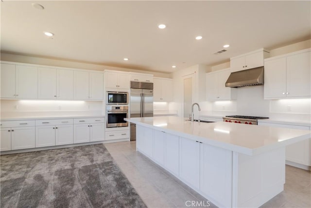 kitchen with white cabinetry, sink, built in appliances, and a kitchen island with sink