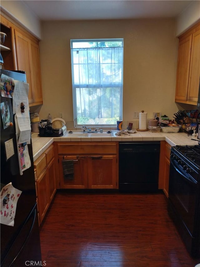 kitchen with sink, tile countertops, dark wood-type flooring, and black appliances