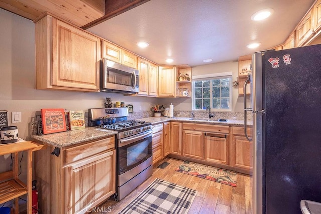 kitchen with sink, stainless steel appliances, light stone counters, light wood-type flooring, and light brown cabinets