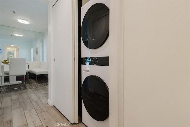 laundry area featuring stacked washer and dryer and light hardwood / wood-style flooring