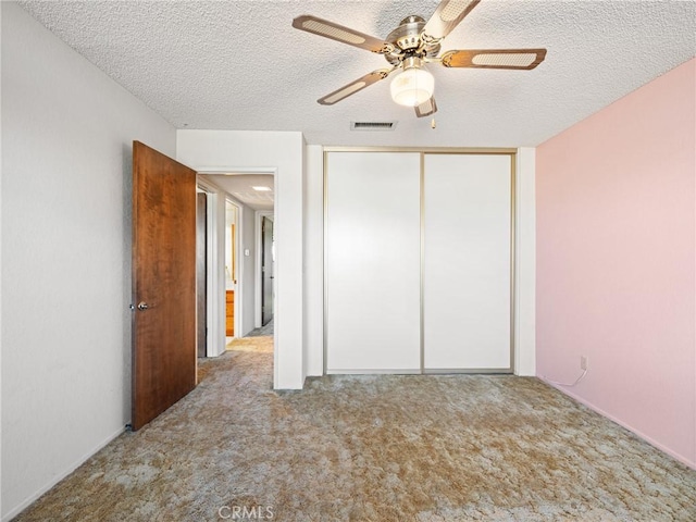 unfurnished bedroom with ceiling fan, light carpet, a textured ceiling, and a closet