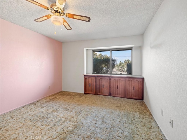 spare room featuring ceiling fan, light colored carpet, and a textured ceiling