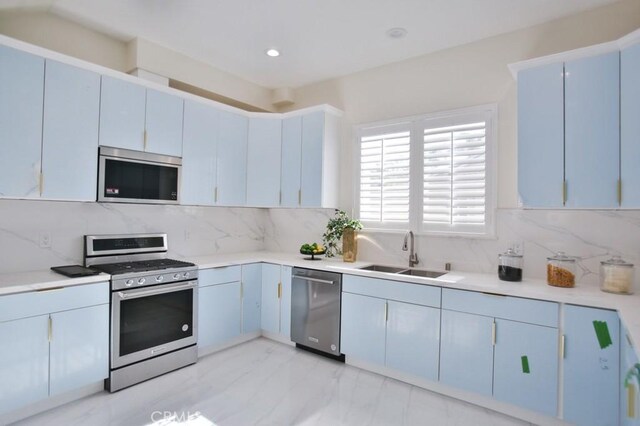 kitchen with stainless steel appliances, blue cabinets, sink, and backsplash