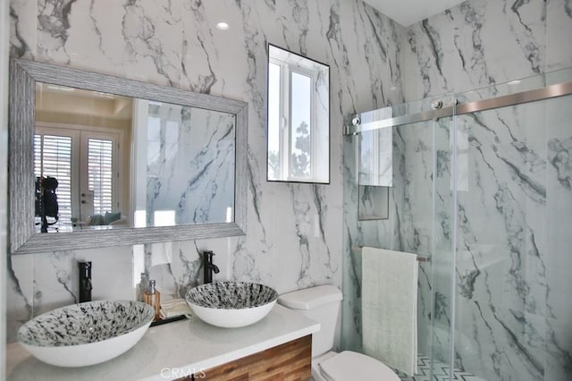 bathroom featuring toilet, a sink, a marble finish shower, and double vanity