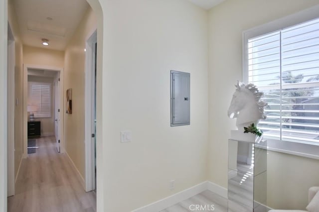 hall with light wood-type flooring, baseboards, electric panel, and arched walkways