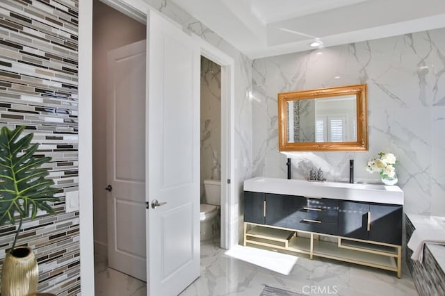 bathroom with marble finish floor, recessed lighting, toilet, vanity, and stone wall