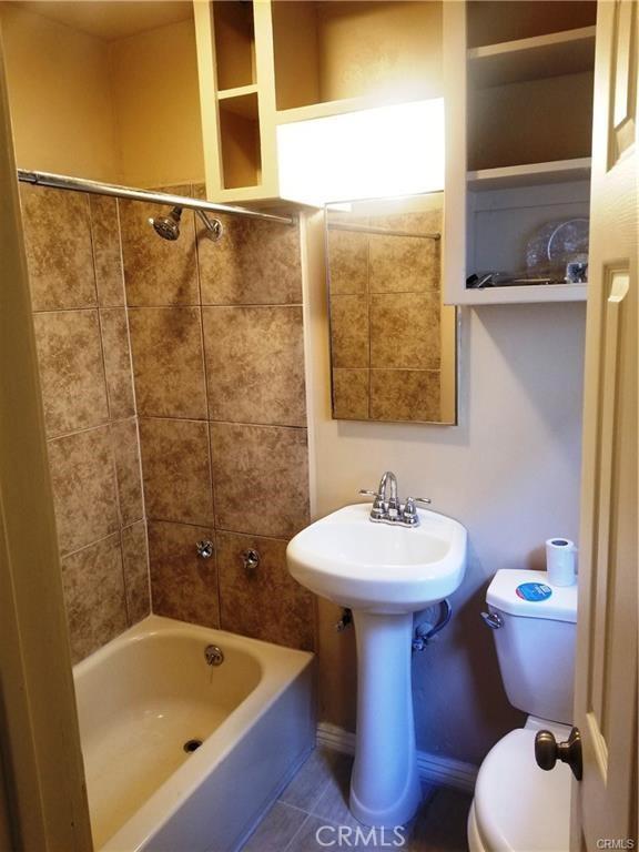 bathroom featuring toilet, tiled shower / bath combo, and tile patterned flooring