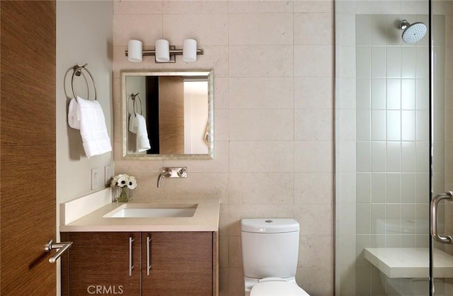 bathroom with vanity, toilet, a shower with shower door, and tile walls