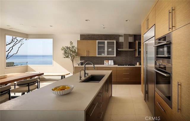 kitchen with sink, wall chimney range hood, an island with sink, and a water view