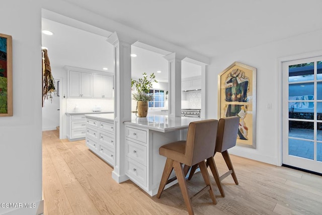 kitchen with light hardwood / wood-style flooring, backsplash, a center island, white cabinets, and ornate columns