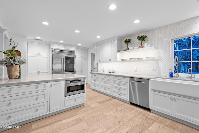 kitchen featuring sink, light hardwood / wood-style flooring, appliances with stainless steel finishes, white cabinets, and decorative backsplash