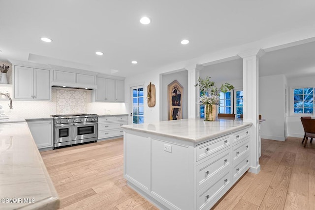 kitchen with light hardwood / wood-style flooring, white cabinetry, double oven range, light stone counters, and tasteful backsplash