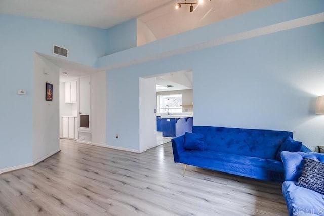 living room with vaulted ceiling, sink, and light wood-type flooring