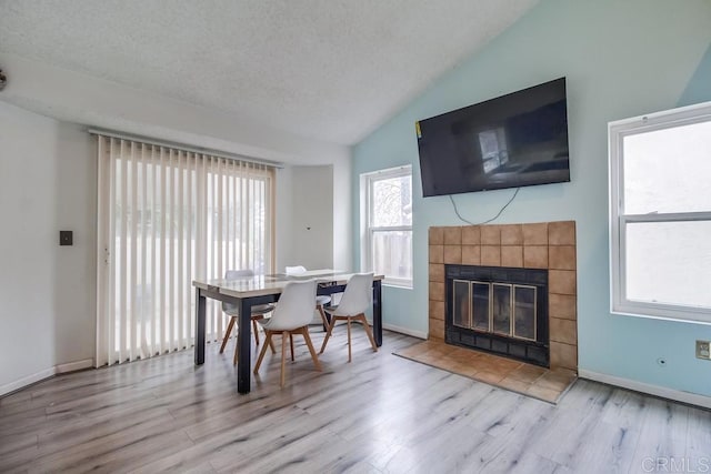 dining room featuring lofted ceiling, a tiled fireplace, and light hardwood / wood-style floors