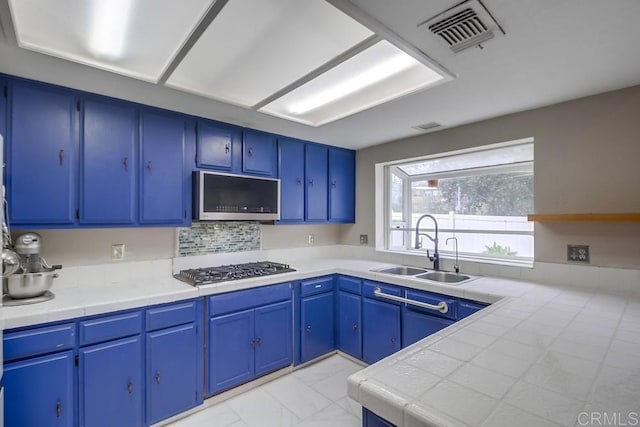 kitchen featuring stainless steel appliances, tile countertops, sink, and blue cabinets