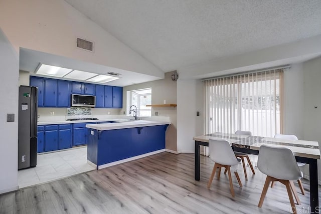 kitchen with appliances with stainless steel finishes, a wealth of natural light, backsplash, kitchen peninsula, and blue cabinetry