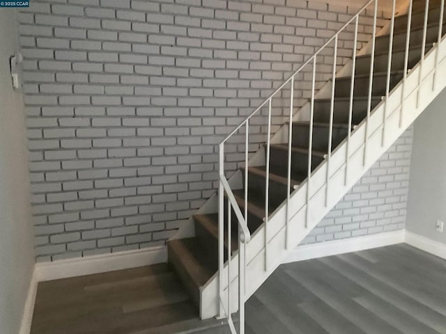 staircase featuring wood-type flooring and brick wall